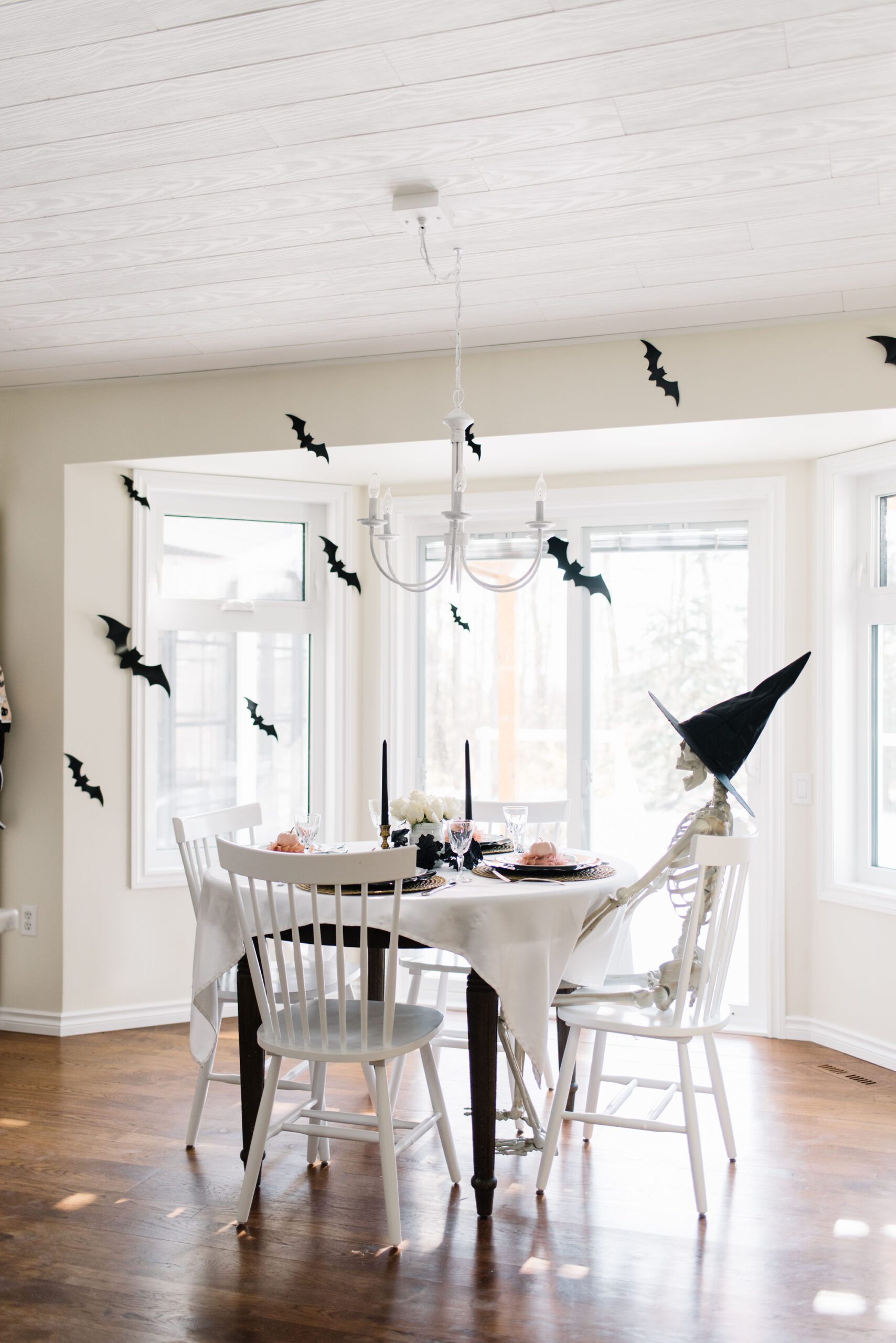 A skeleton sits at a halloween table with bats hung above