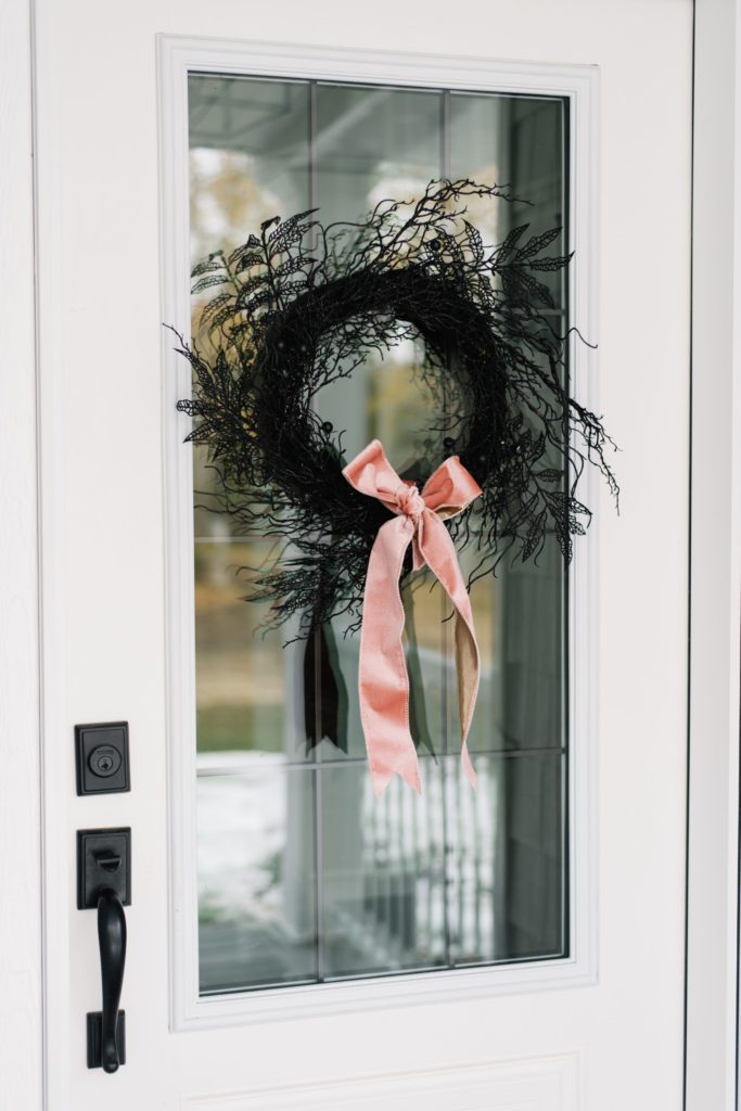 A simple black twig wreath looks luxe with a pink velvet bow for Halloween