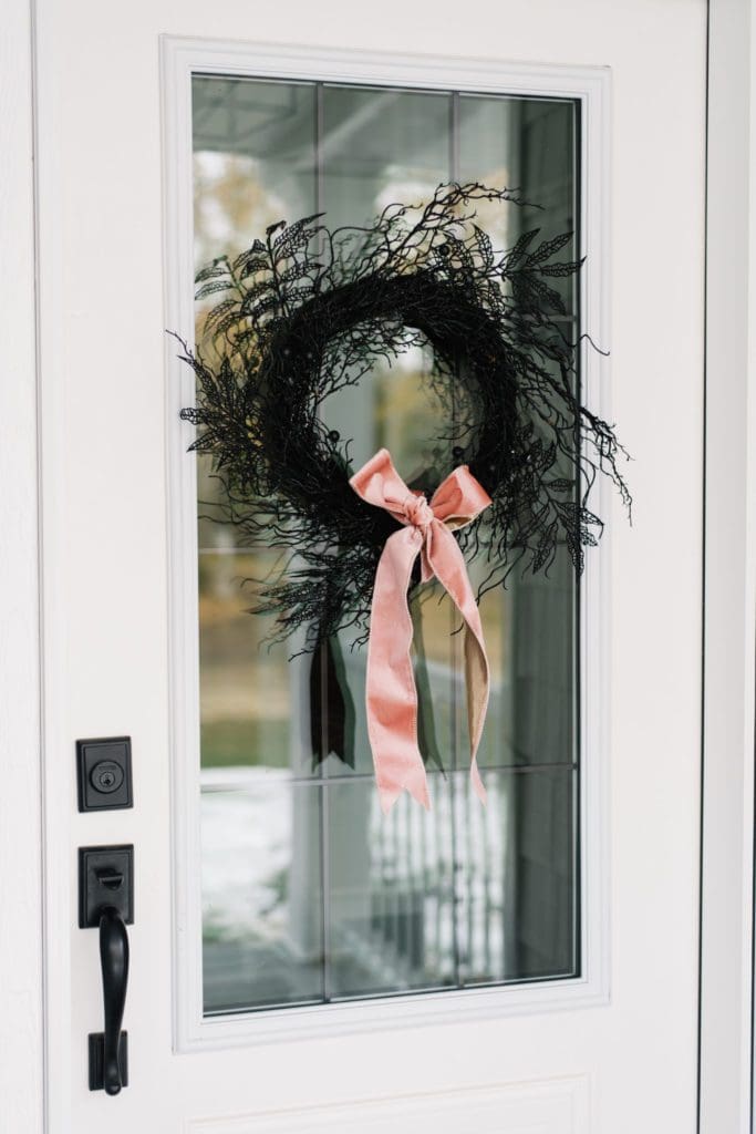 A simple black twig wreath looks luxe with a pink velvet bow for Halloween