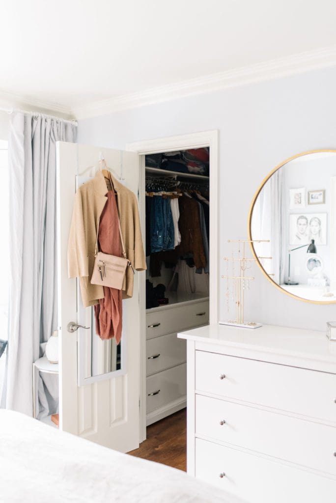 A small master bedroom closet with a dresser added for storage and clothing hanging on the door.