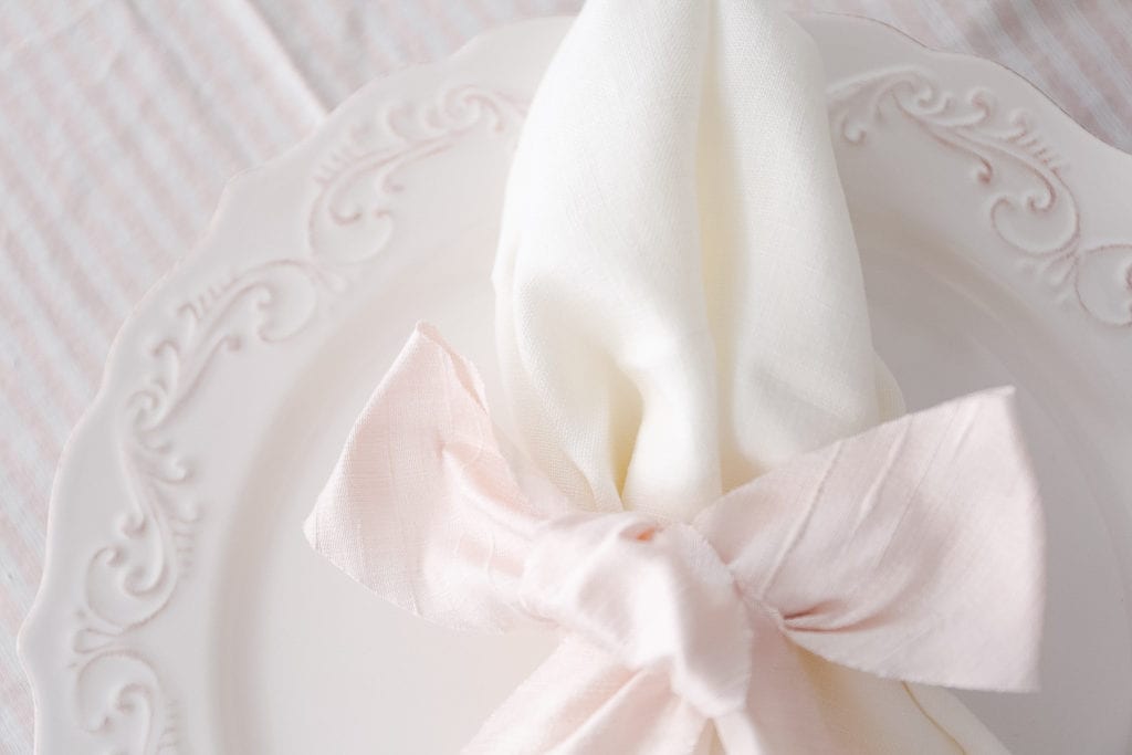 A close up of a napkin tied with pink silk ribbon