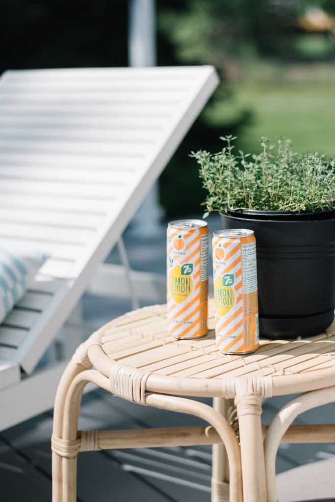 drinks sit on a rattan outdoor side table beside a pot of herbs