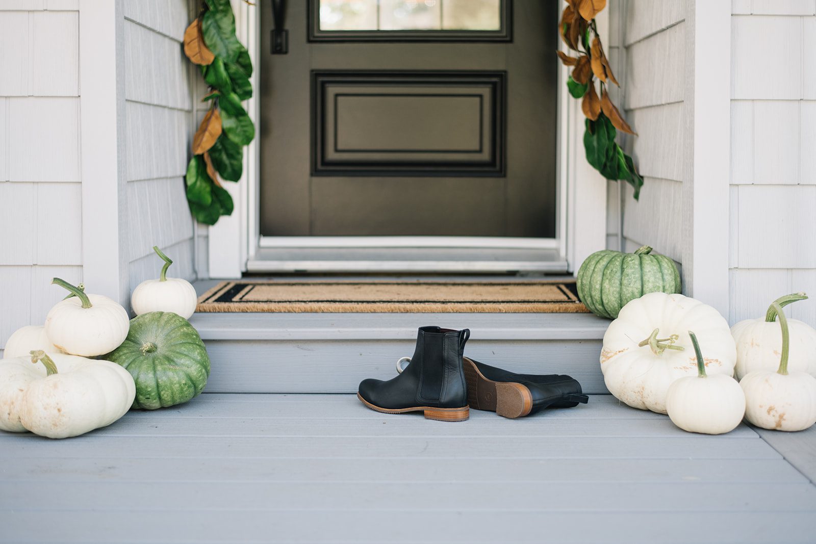 boots sit beside pumpkins in front of fall front door