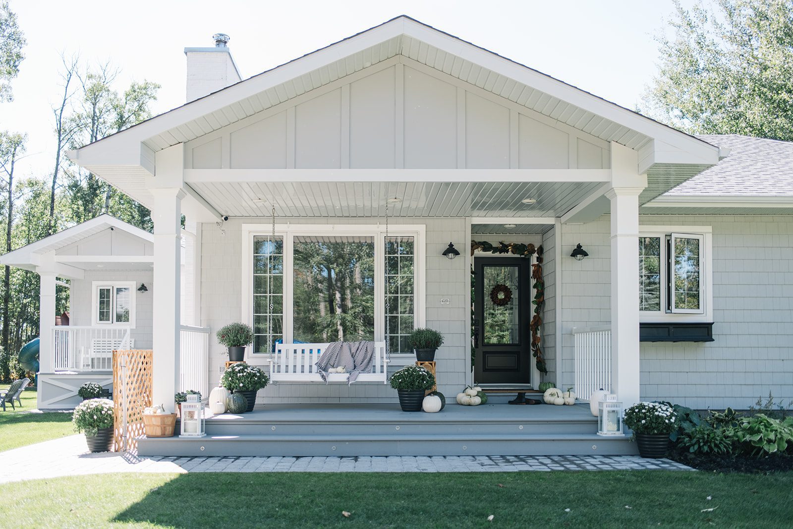 Modern country farmhouse with grey shingles and board and batten, black door and porch swing