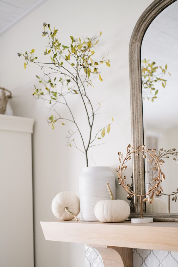 A vase with large branches with mini white pumpkins
