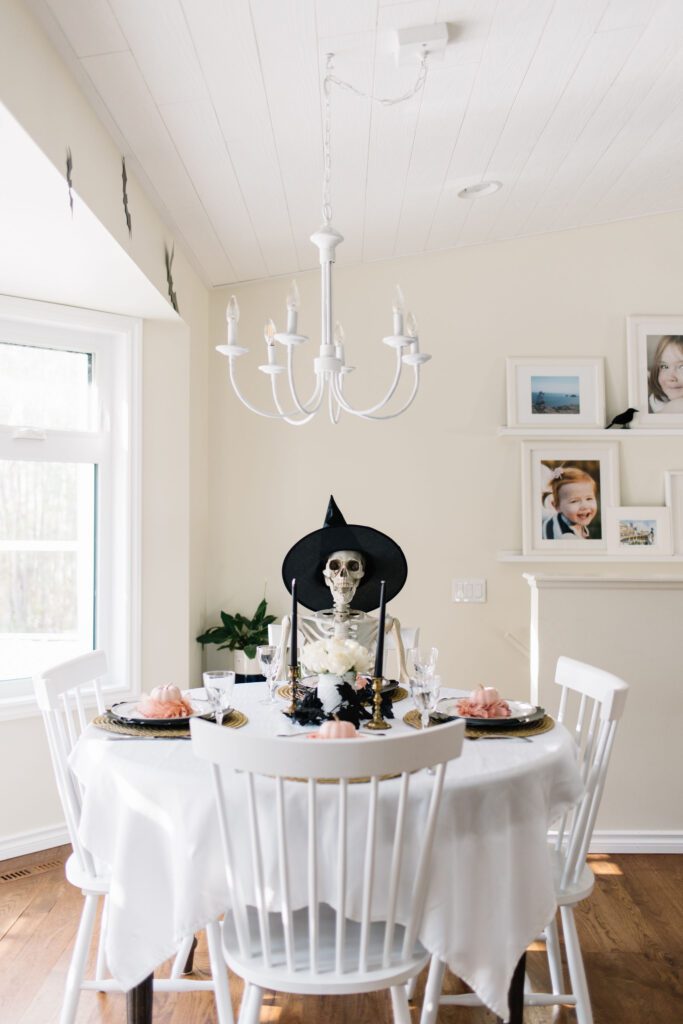 A Skeleton in a witch hat sits at a table decorated for Halloween