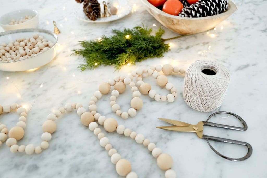 Simple wood bead DIY Christmas garland beside scissors and string