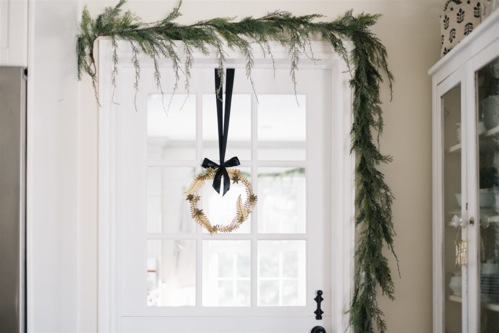 A wreath tied with black ribbon to a door under cedar garland