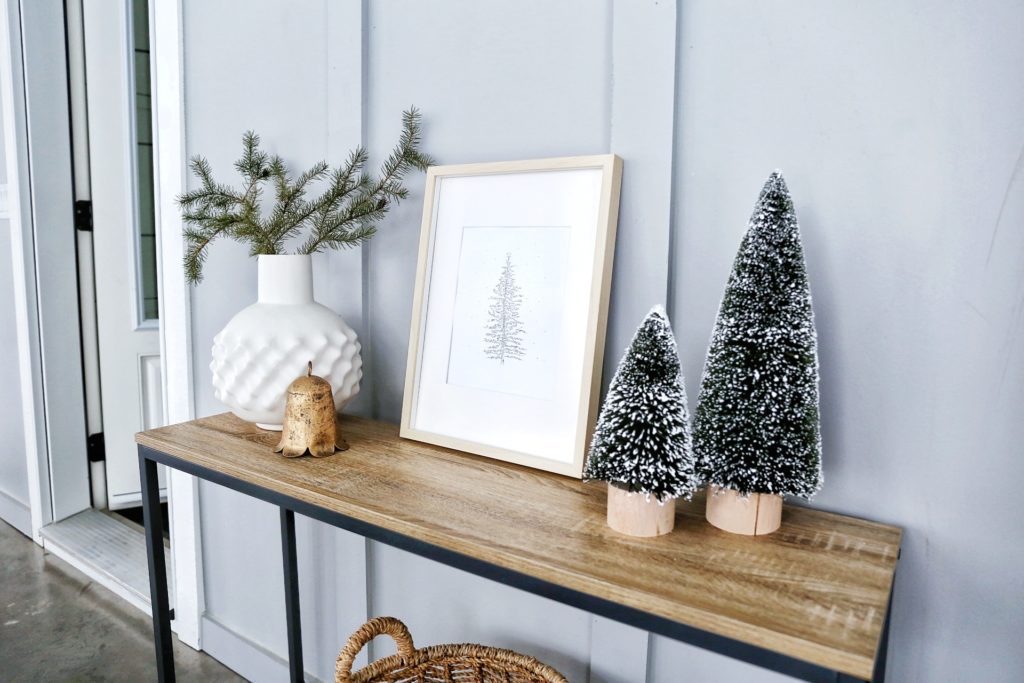 Framed print of a Christmas tree on a console table beside winter greens