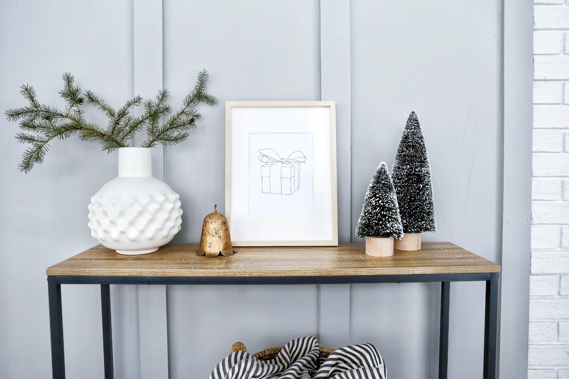 framed print of a present sits on a console table beside Christmas trees and a brass bell