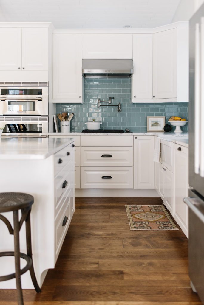 A kitchen with a wood floor, white cabinets and blue backsplash
