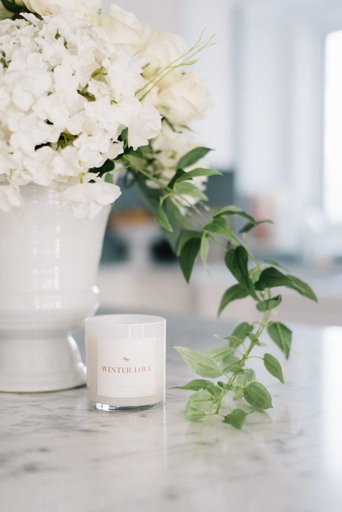 A vase of flowers with trailing greens and a winter candle