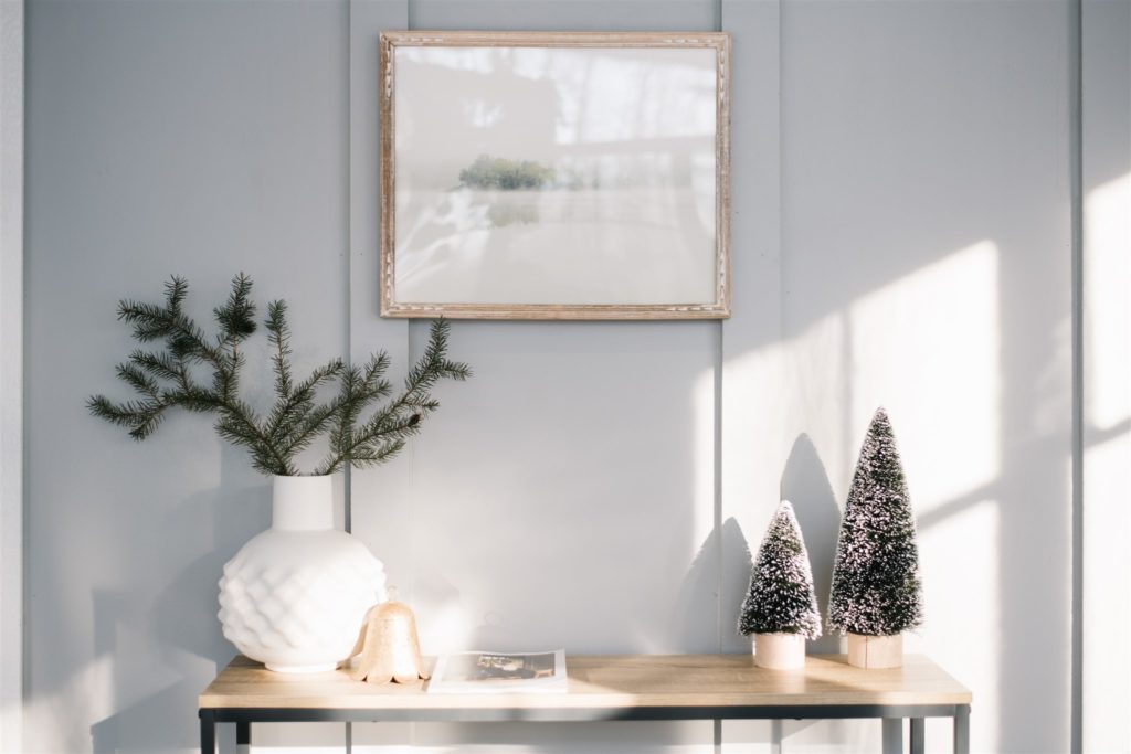 framed painting above console table with christmas trees and winter greens