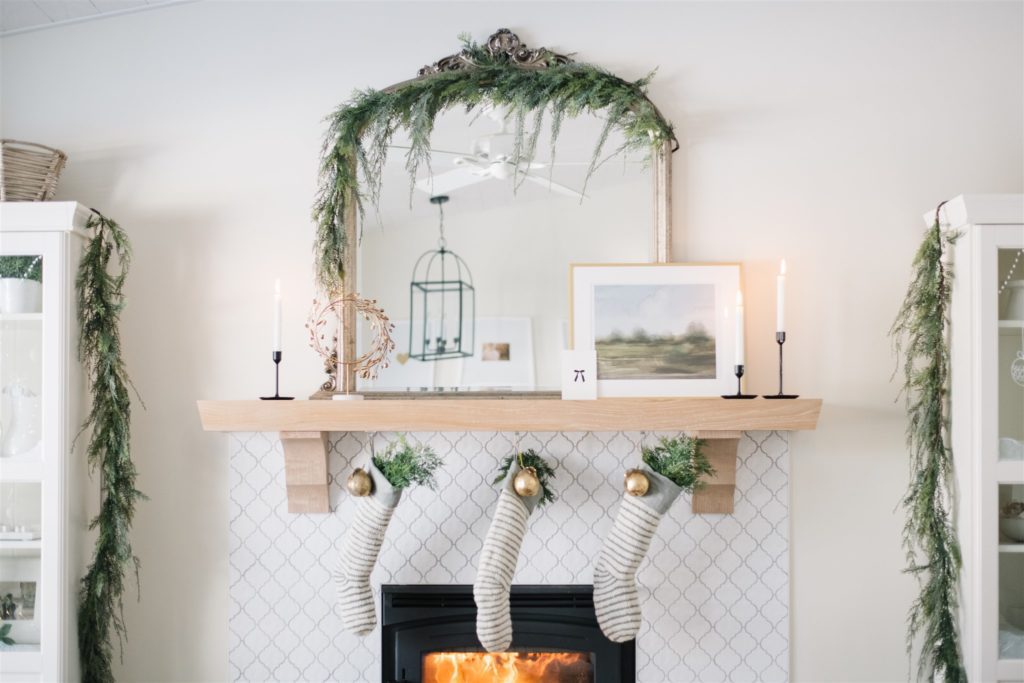 Neutral scandinavian Christmas mantle decor with hanging stockings and green garland on the mirror