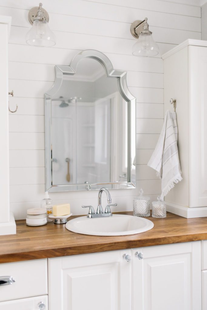 Updated bathroom vanity with wooden countertops and large silver mirror