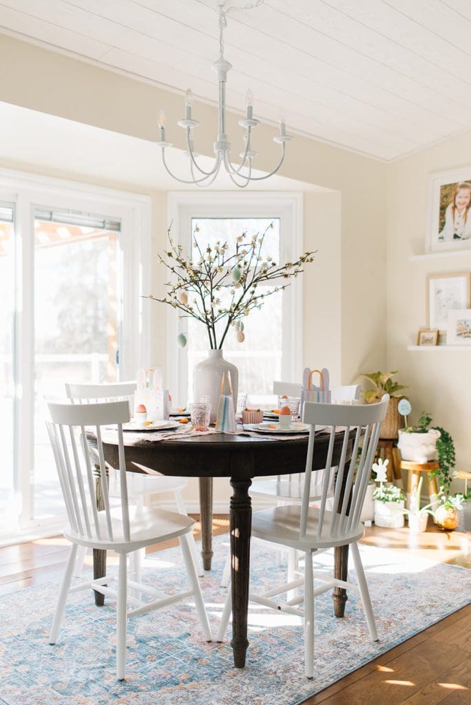 A dining room table with a vase filled with pussy willows and easter decorations