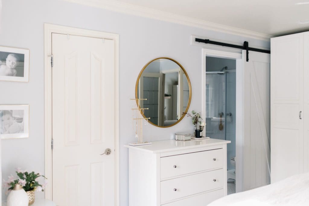 dresser with round mirror above beside sliding door access to master bathroom