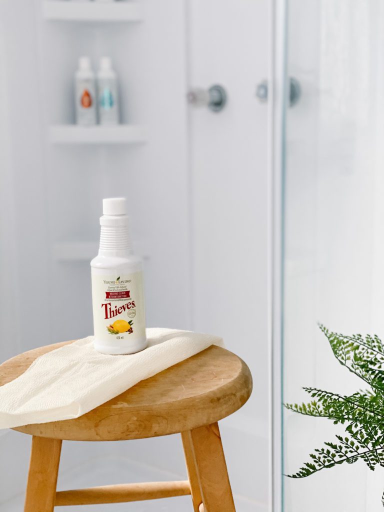 A bottle of cleaner on a stool in front of a glass shower