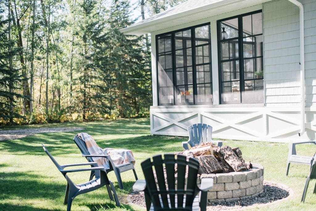 Lawn chairs around a firepit in front of a house with large black windows