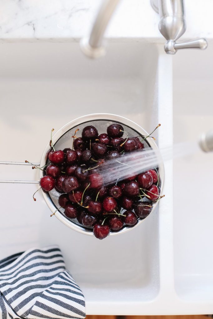 A sieve of fresh cherries under running water
