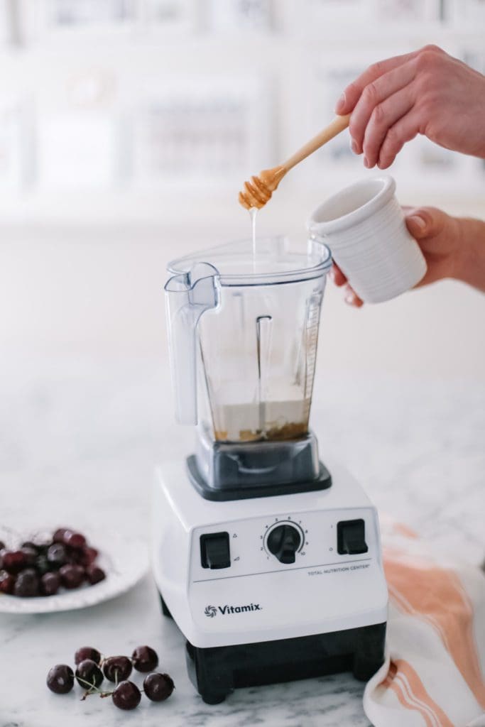 pouring honey into a white vitamix blender