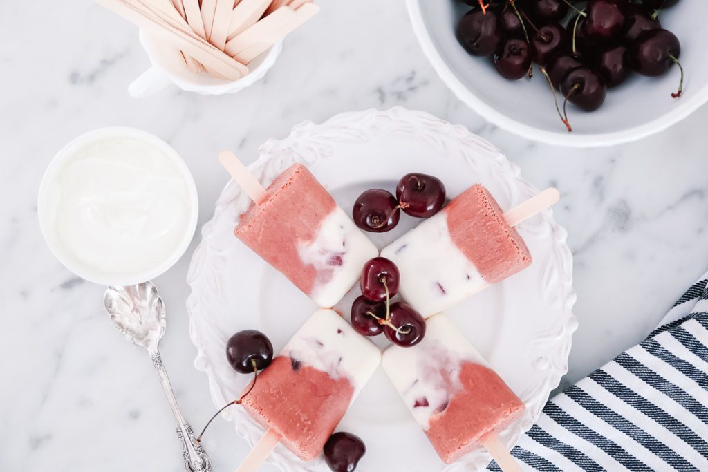 creamy cherry popsicles on a plate with fresh cherries