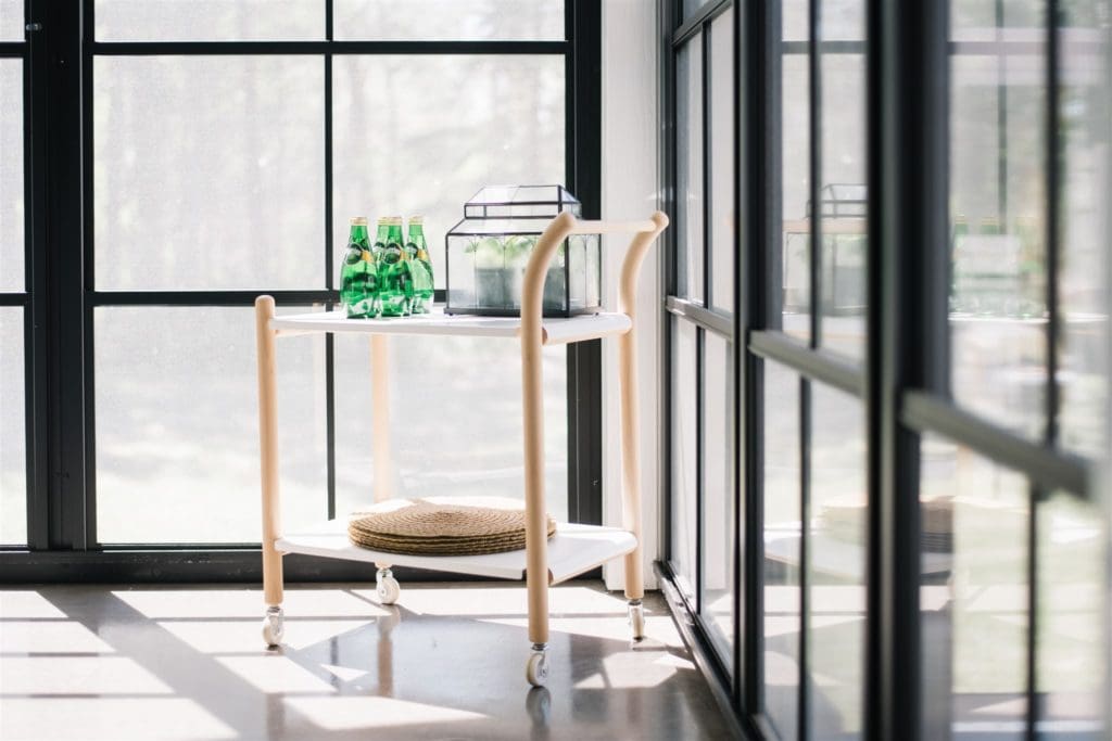 a  white and wood bar cart sits in the corner of a sun room