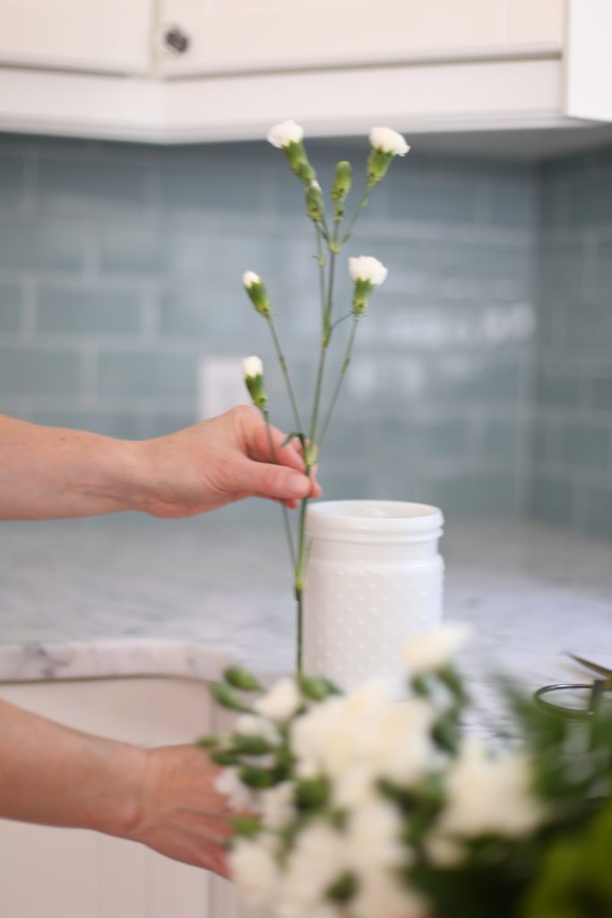 holding flower stems up beside a vase to see how long to cut the stem