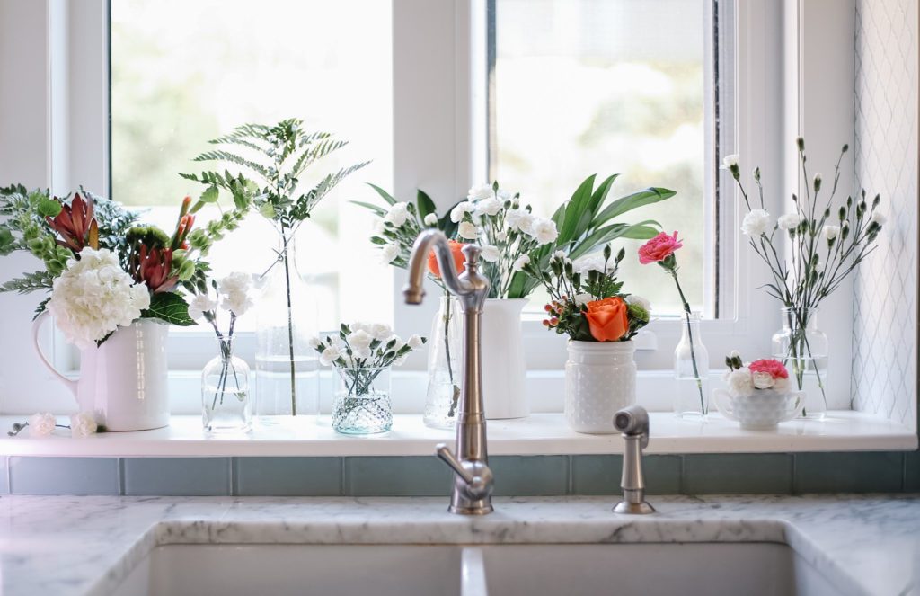 multiple floral arrangements lined up on kitchen window sill