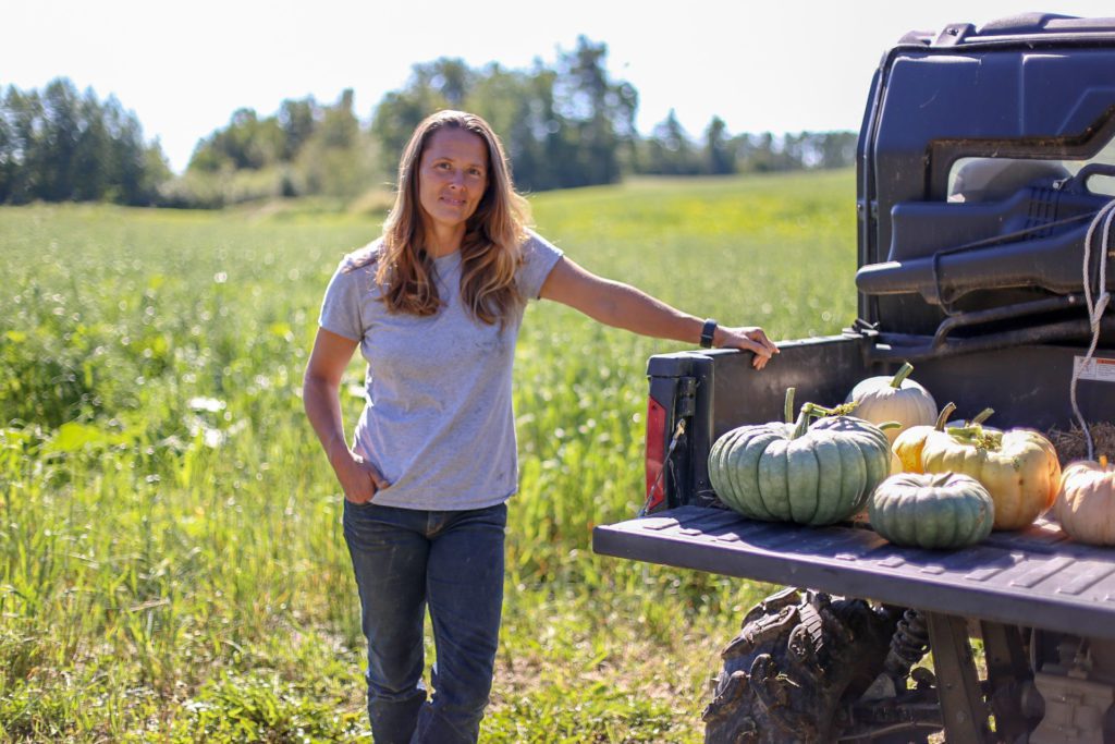 A woman standing in a field with pumpkins in the back of a truck