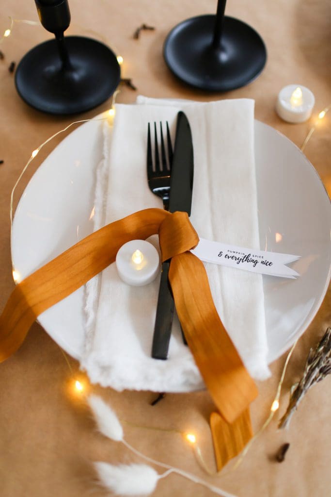 place setting with white plate and napkin, black cutlery and bronze silk ribbon