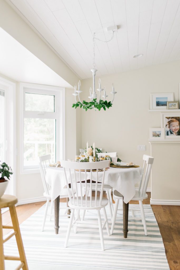 A dining room table with greenery on the chandelier above it