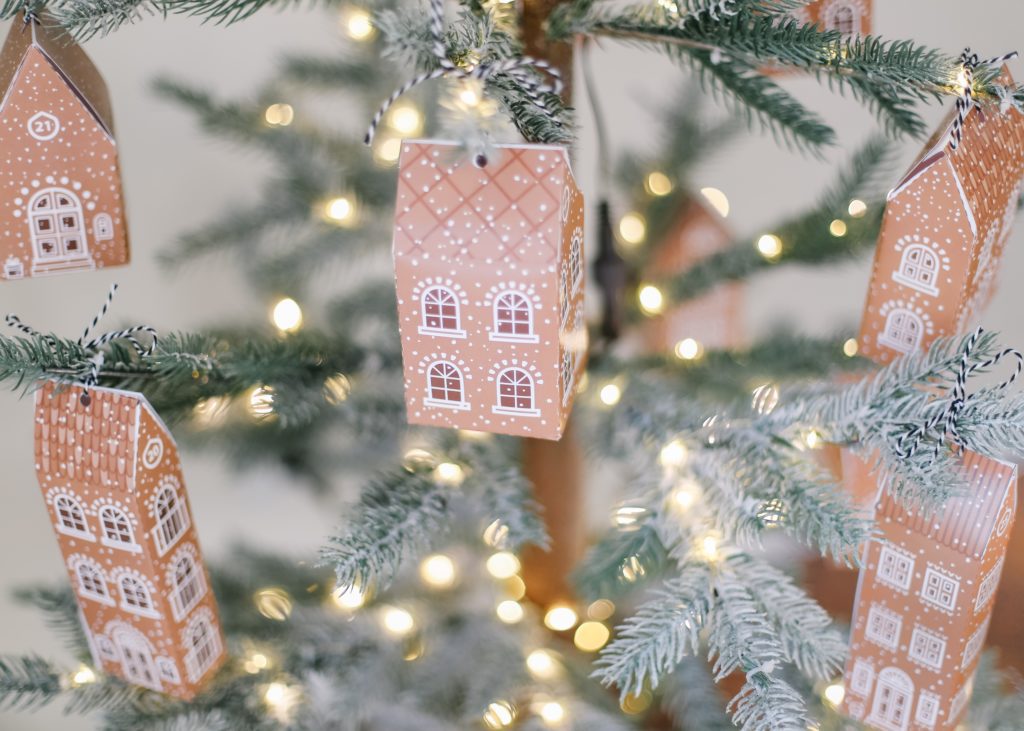tiny gingerbread house gift box hung on a lit Christmas tree