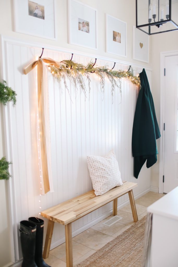 A front entry with greens, lights and ribbon hung across the coat hooks