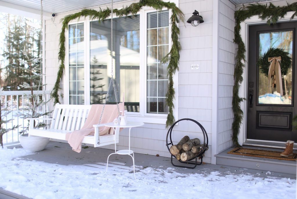 A window hung with garland and a blanket on a front porch swing