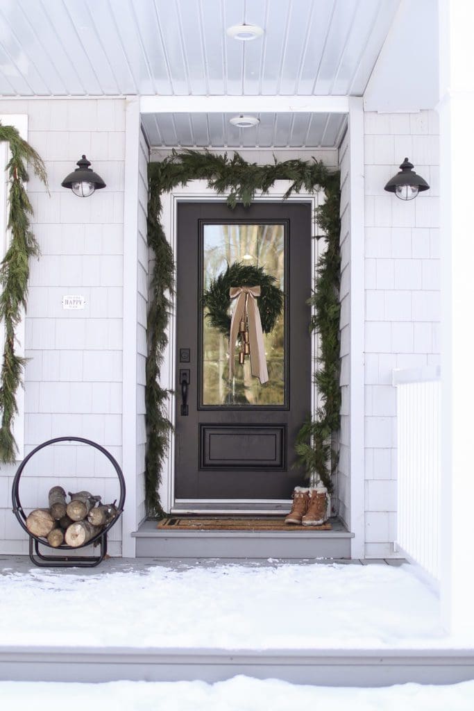 A black front door decorated for Christmas with fresh garland and wreath