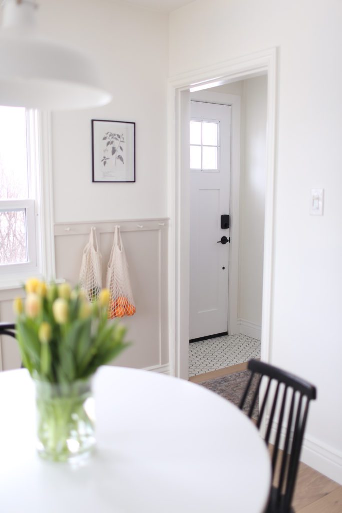A view through the dining room to the white front door and black and white floor tile in the front entrance.
