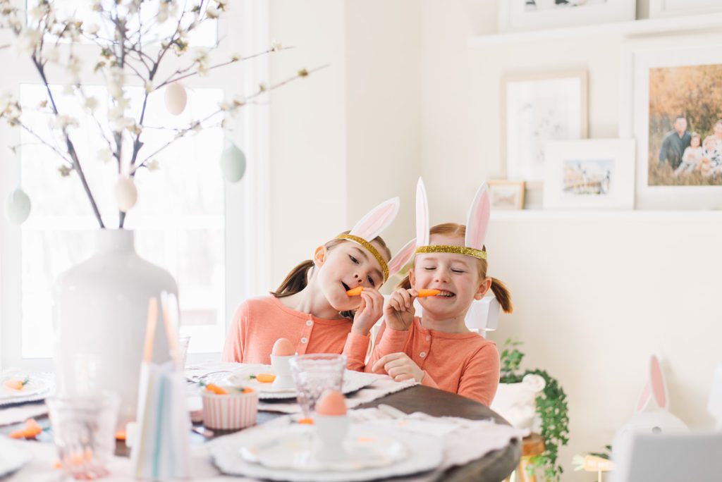 2 little girls pretend to eat carrots in orange jumpers and bunny ears