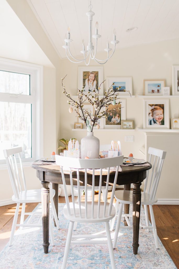 A round wooden dining room table with white chairs set up as a kids easter tablescape with bunny themed accessories