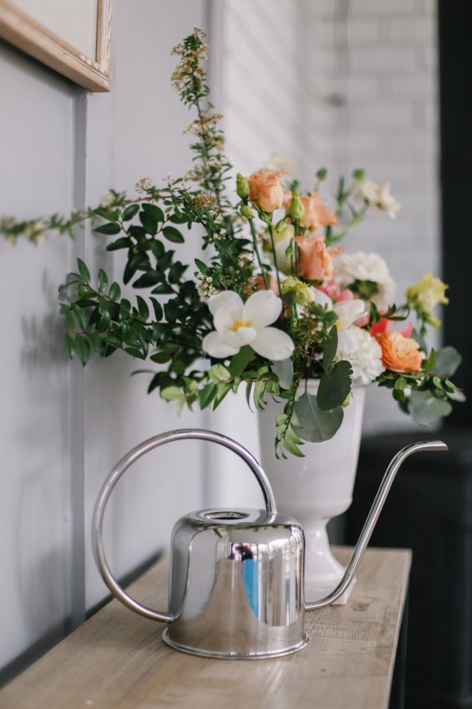 A vase of flowers on a table with a silver watering can