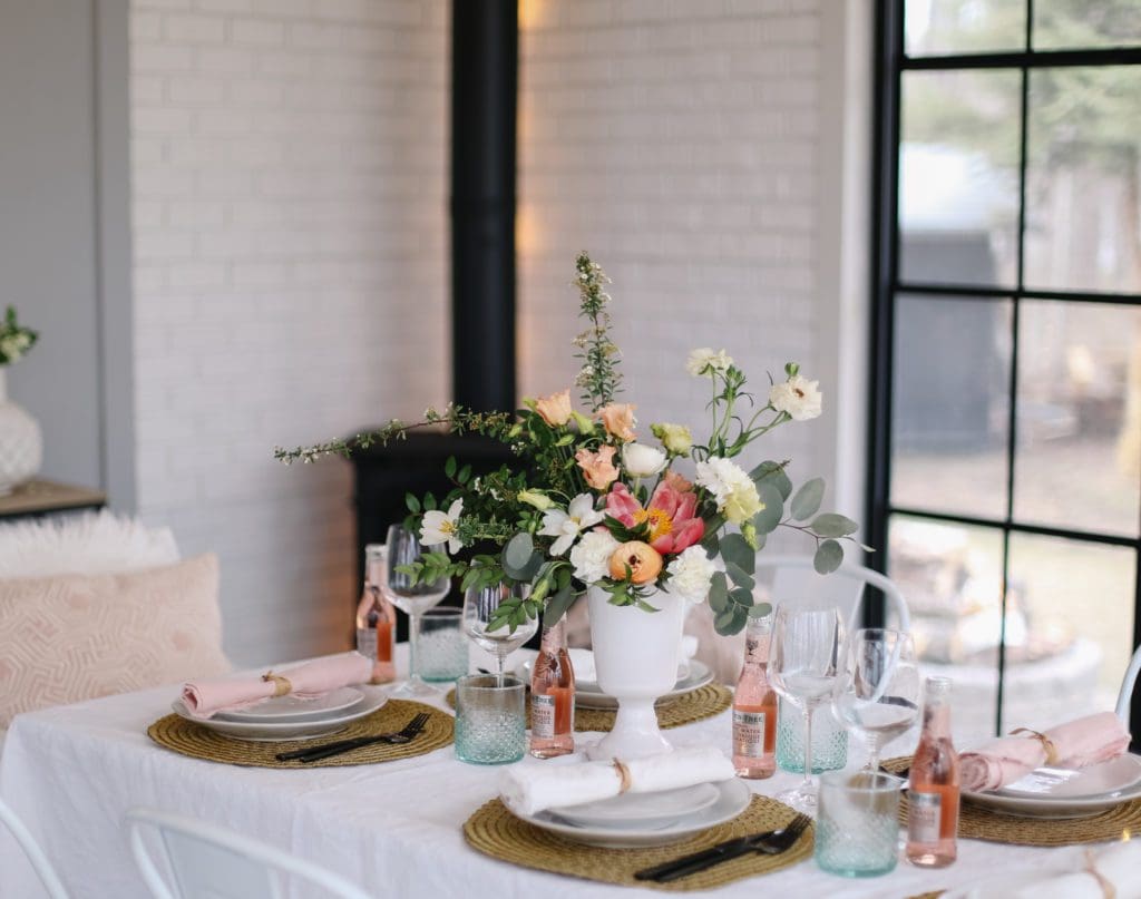 A vase of flowers on a pretty mother\'s day tablescape with pink bottles and green glasses