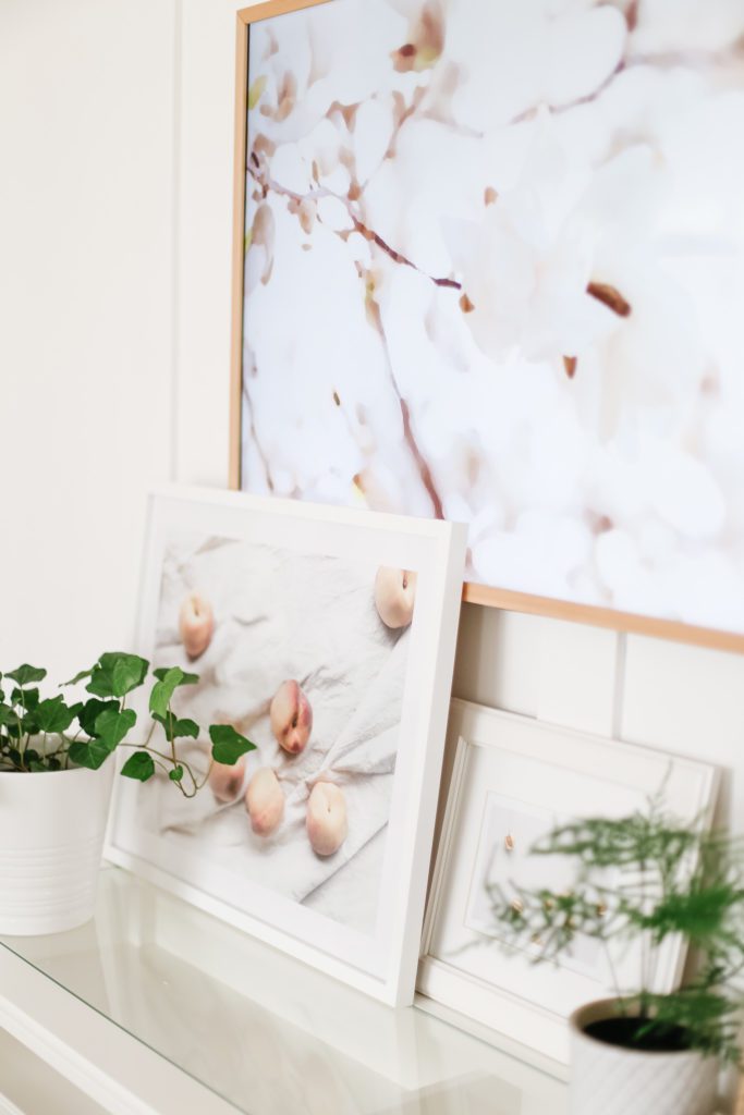 An art print of peaches displayed on a console table under a TV
