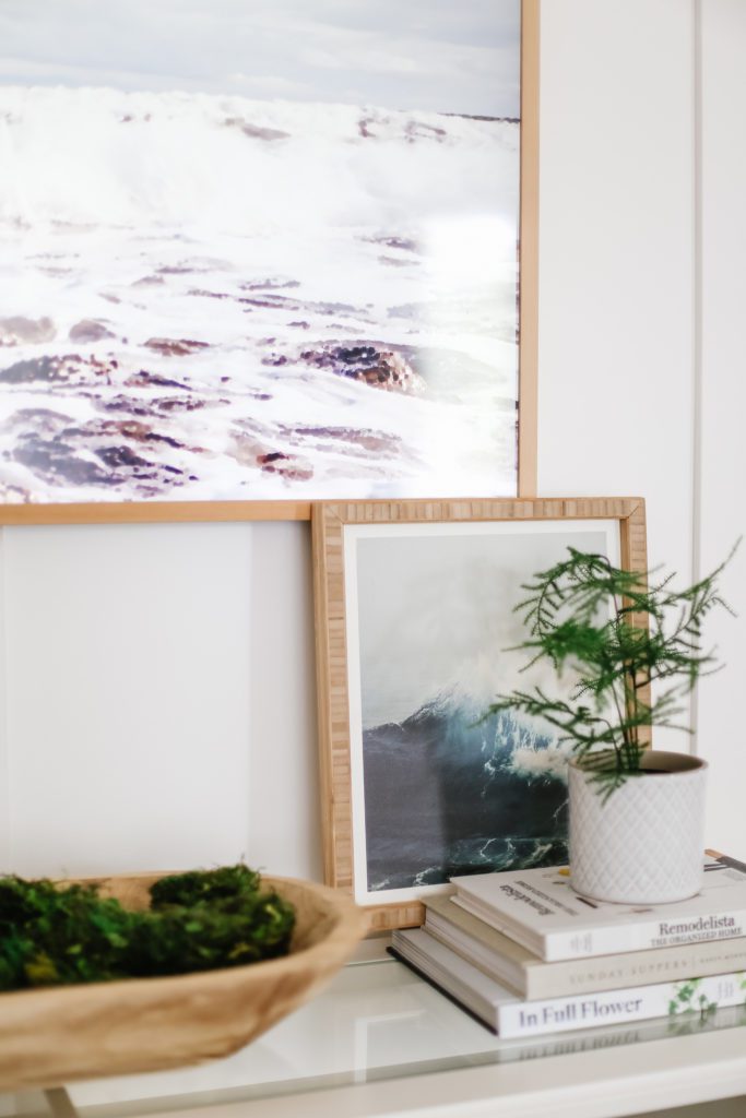 Samsung Frame TV displayed above a painting of the ocean and potted plant sitting on some books