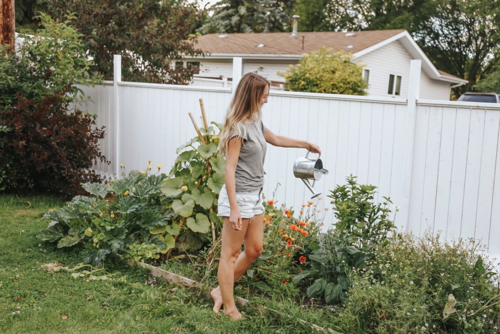 A woman watering plants standing in front of a white fence.