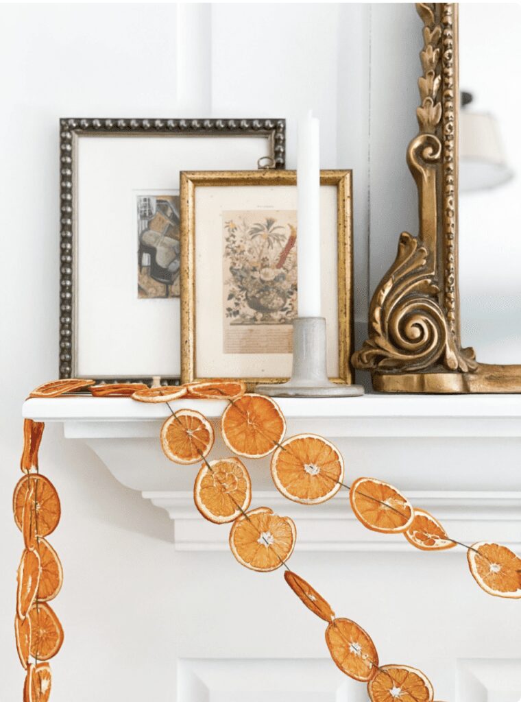 orange garlands hanging on the corner of a white mantle below picture frames