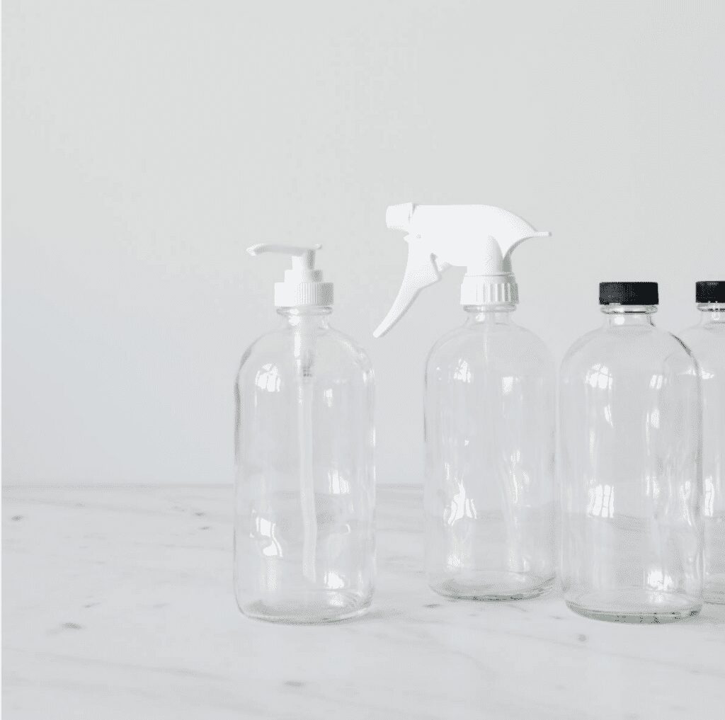 Clear glass spray bottles with white and black tops on a marble counter