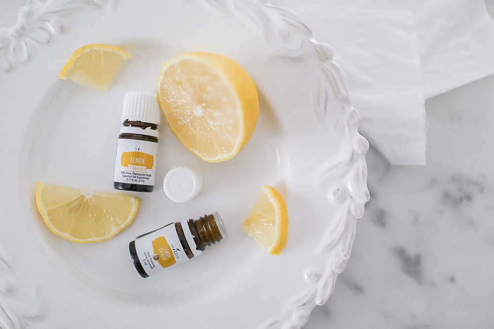 Bottles of Lemon Essential Oil lying on a plate besides slices of lemon and tissues