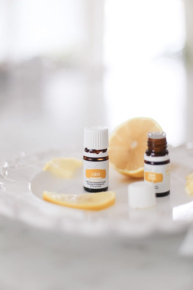 Bottles of lemon essential oil sit on a white plate with fresh lemon slices